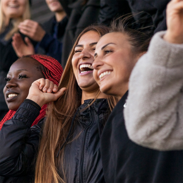 Un groupe de jeunes femmes souriantes et joyeuses exprime leur enthousiasme. Elles sont vêtues de vestes noires et se tiennent debout, applaudissant et riant ensemble, créant une atmosphère de camaraderie et de célébration.